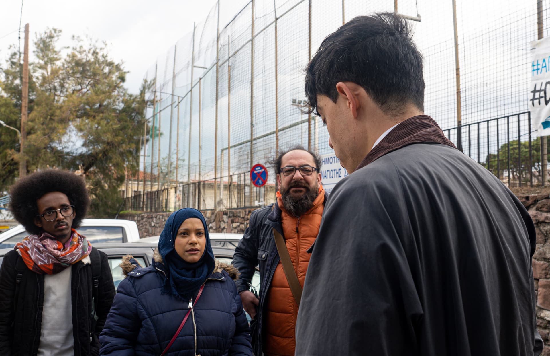 Seán stands with his back to the camera and talks to a group of people outside the courthouse.